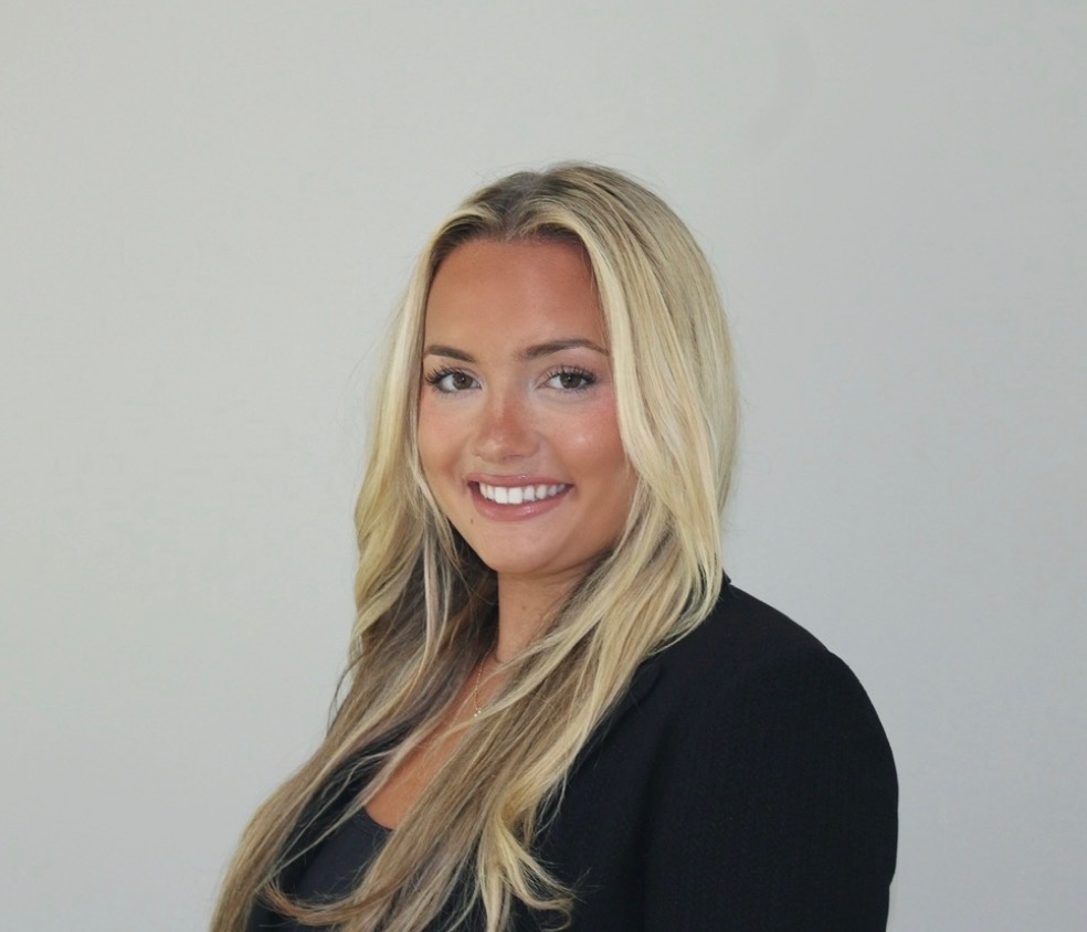 Headshot of a woman with blonde hair wearing a black top, standing in front of a gray background