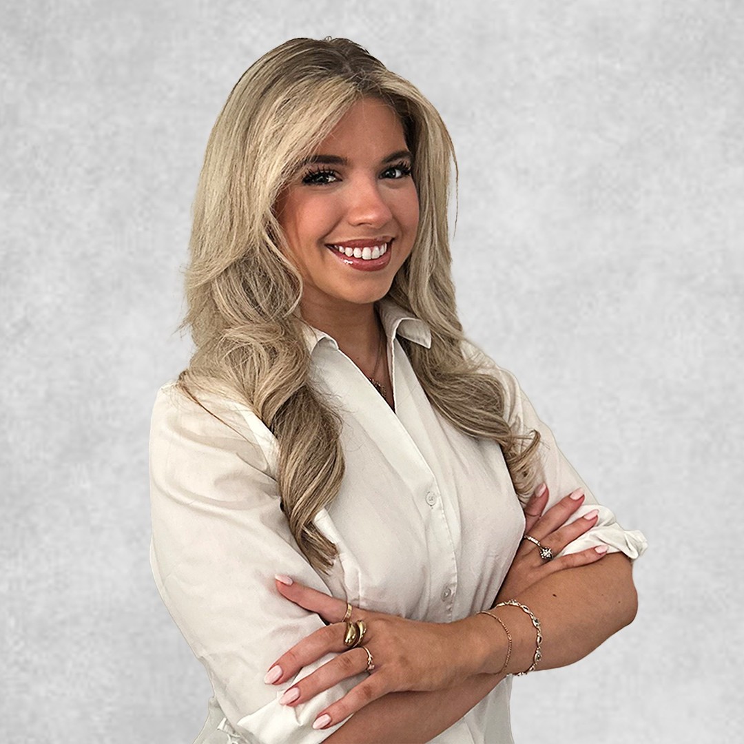 Headshot of a woman with blonde hair wearing a white blouse, standing in front of a gray background
