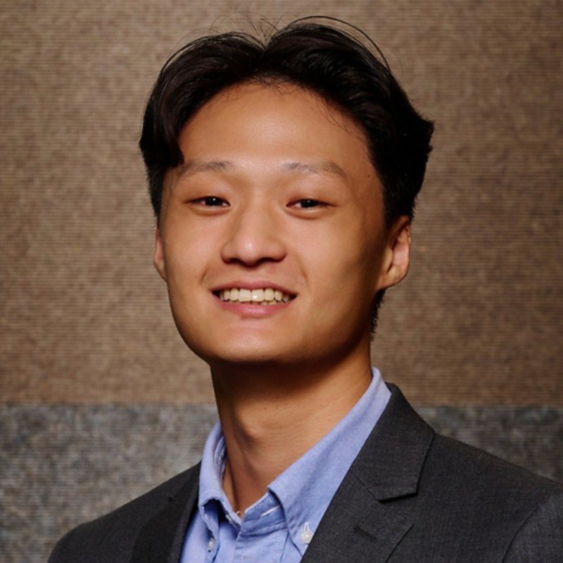 Headshot of a man wearing a suit jacket, smiling in front of a blurred background