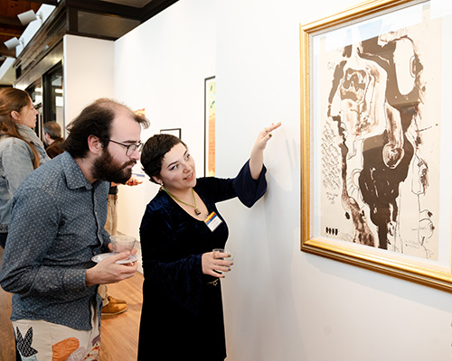 Patrons look at a piece at the exhibit, "Abstract Activism: Sam Maitin's Philadelphia."