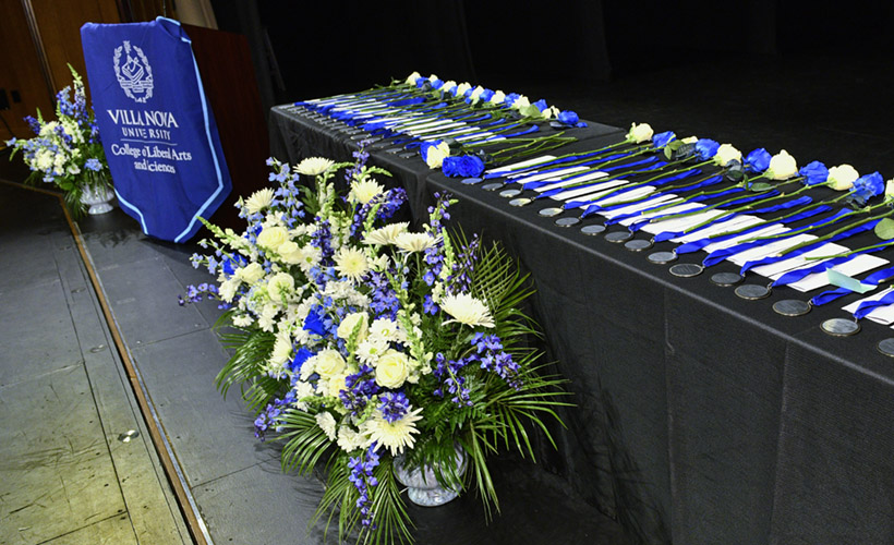 A table with medallion awards on a stage with blue and white flowers.
