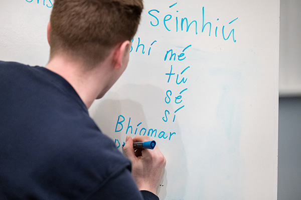 A student writes in Gaelic on the white board.