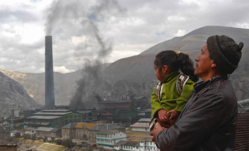 man holding a child looking down onto a smoke stack with black smoke