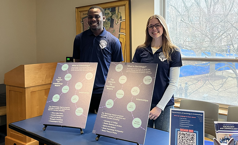 Students stand at a table behind posters about the sociology and criminology majors.