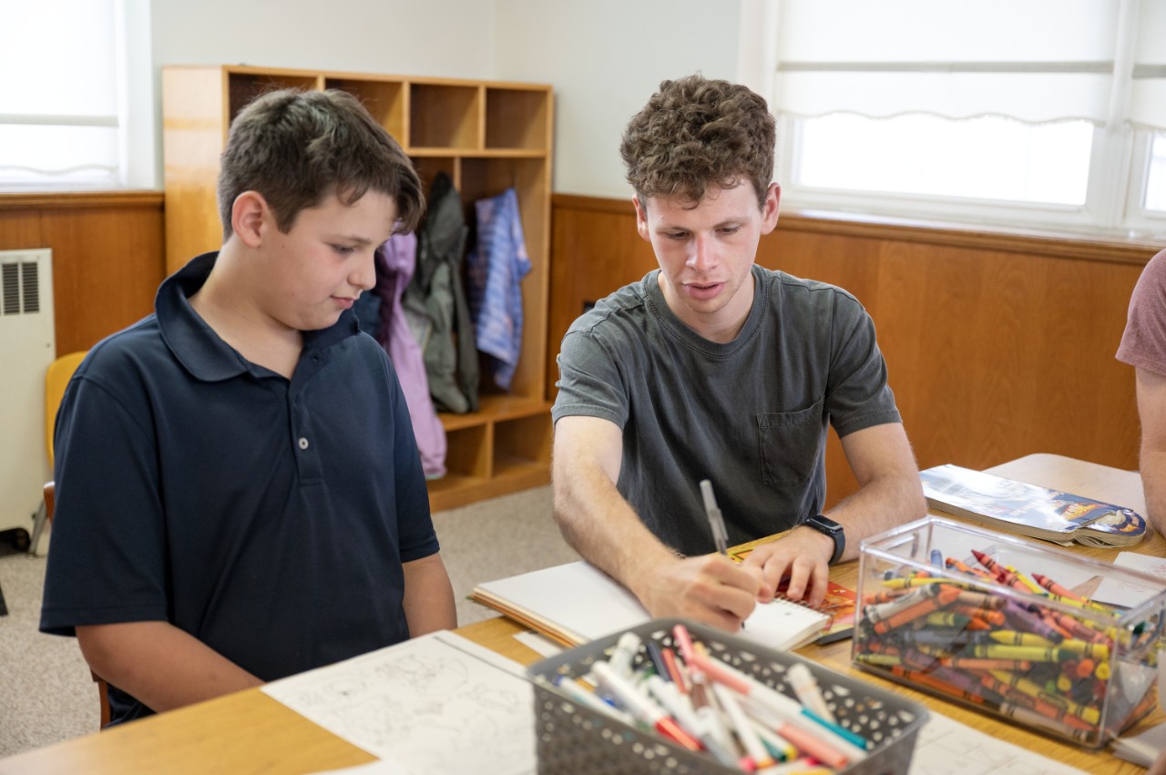 A Villanova student coloring with a young boy at a table