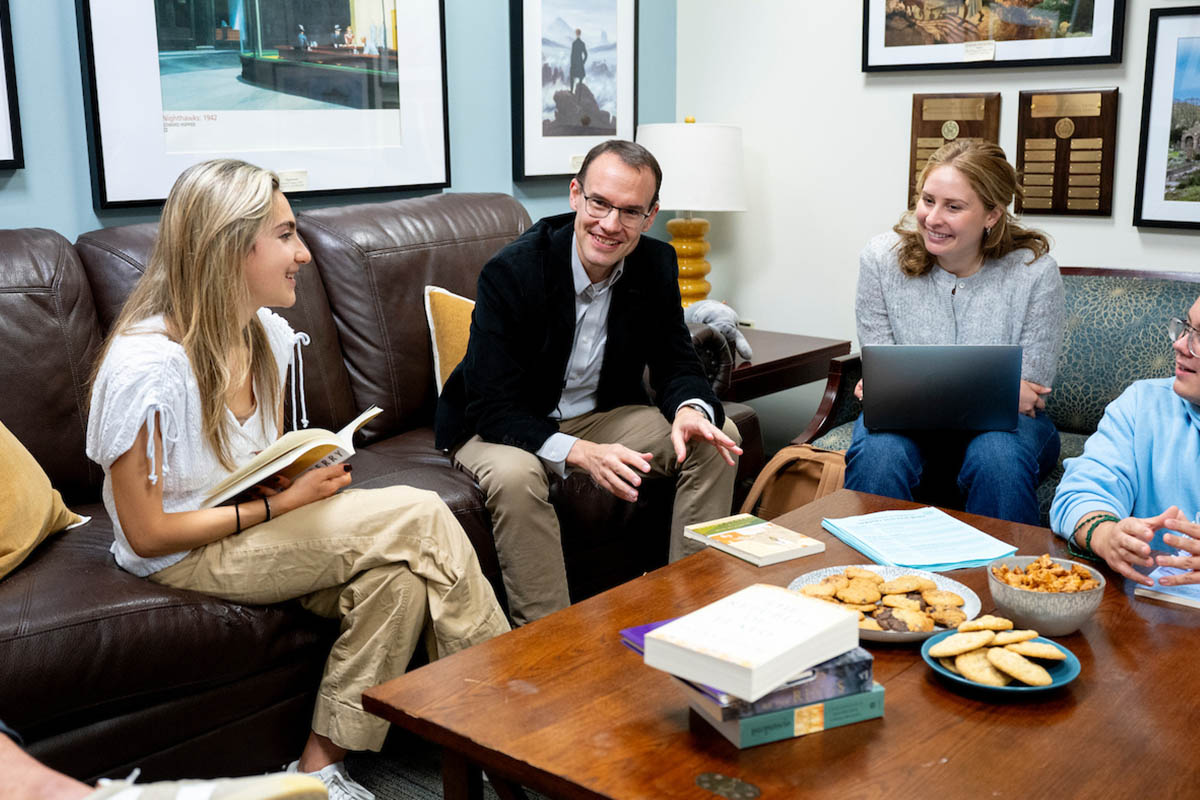 Students gathered around a table talking and holding books