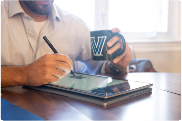 man writing on a tablet holding a Villanova V mug