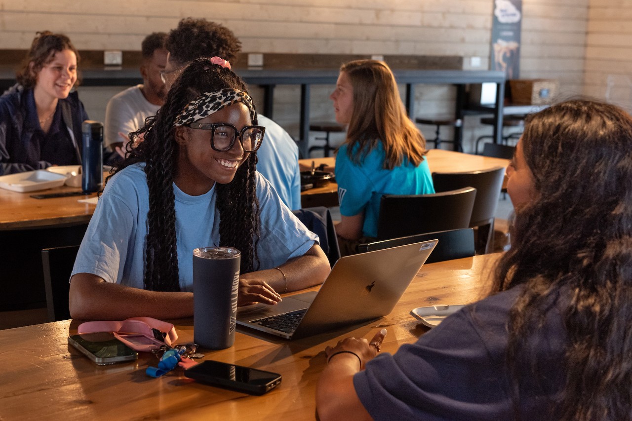 A student works on a computer with a coffee at Holy Grounds.