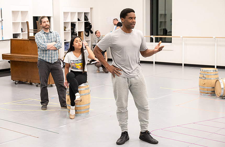 Villanova Theatre students, one of whom is sitting on a barrel, rehearse a scene from in the Mullen Center