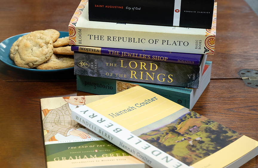A stack of great books sits on a wooden coffee table next to a plate of cookies.