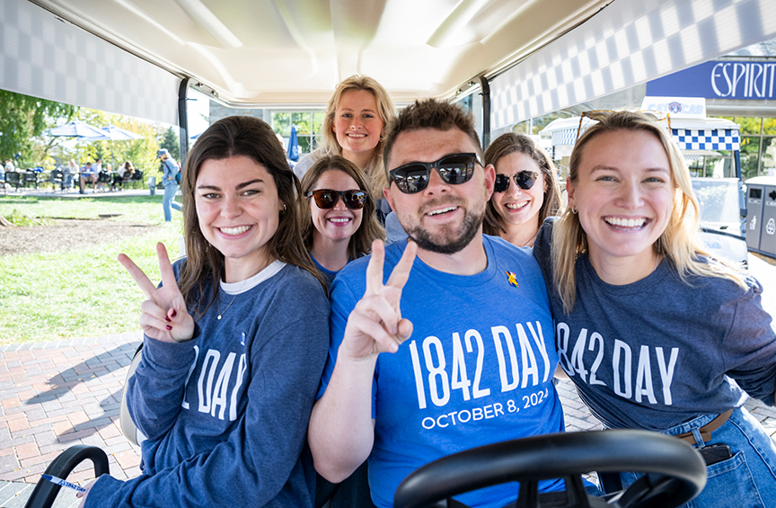 Six Villanovans wearing blue 1842 T-shirts smile directly at the camera sitting in a Cat Cab.