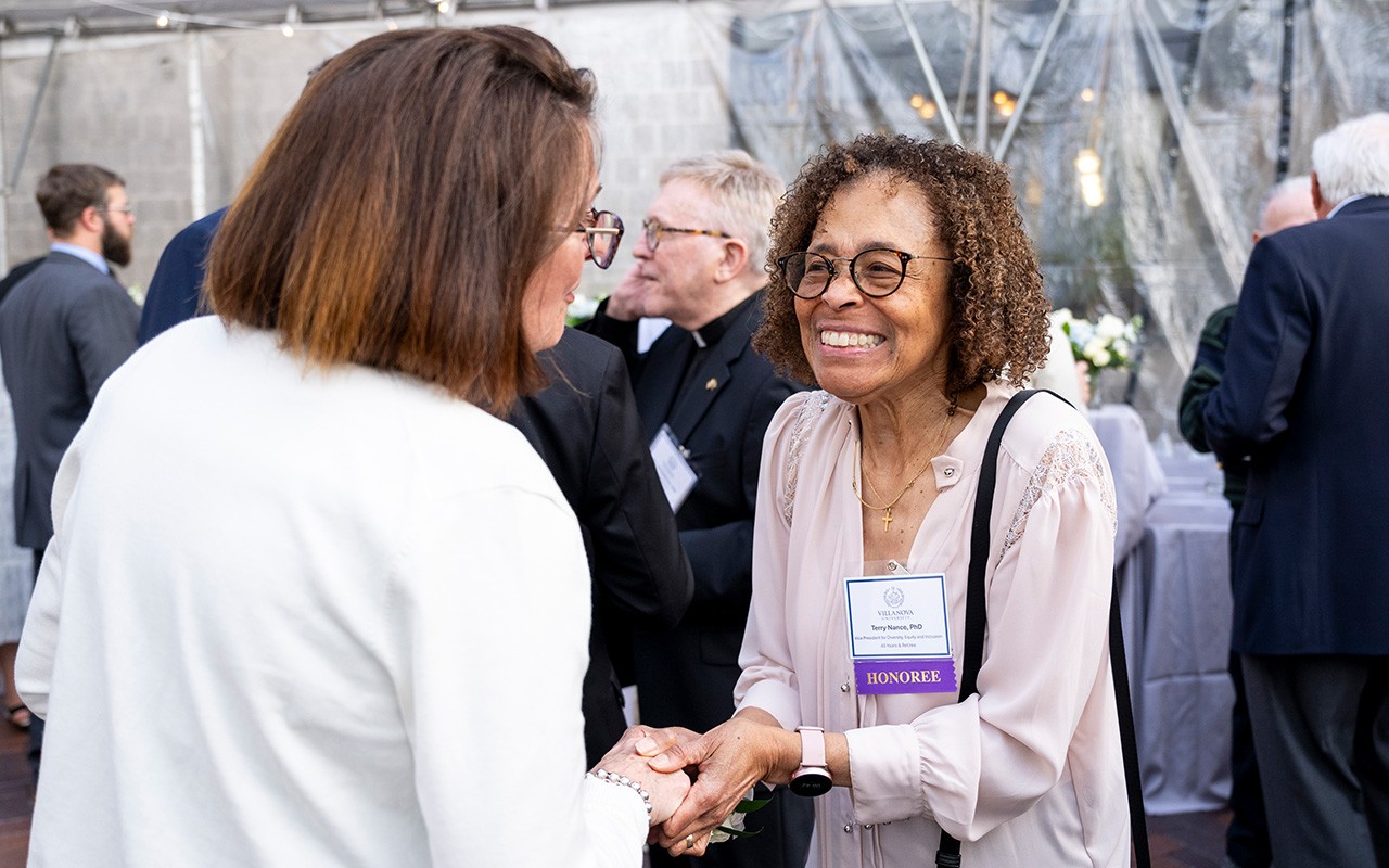 A smiling Teresa Nance places her hand on the top of another woman's hand at a celebratory event.