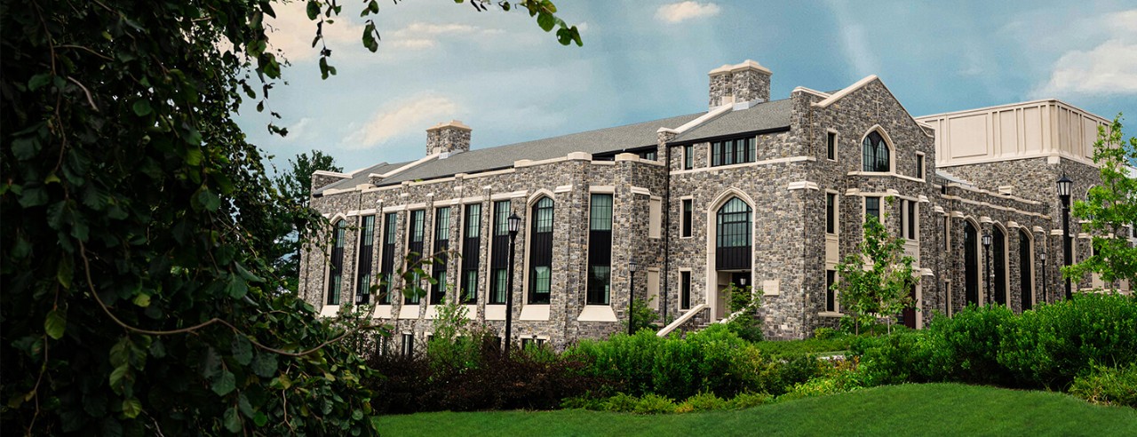 Exterior view of Drosdick Hall at Villanova University, surrounded by greenery including shrubs and young trees, under a clear blue sky, with the rooftop garden walls visible.
