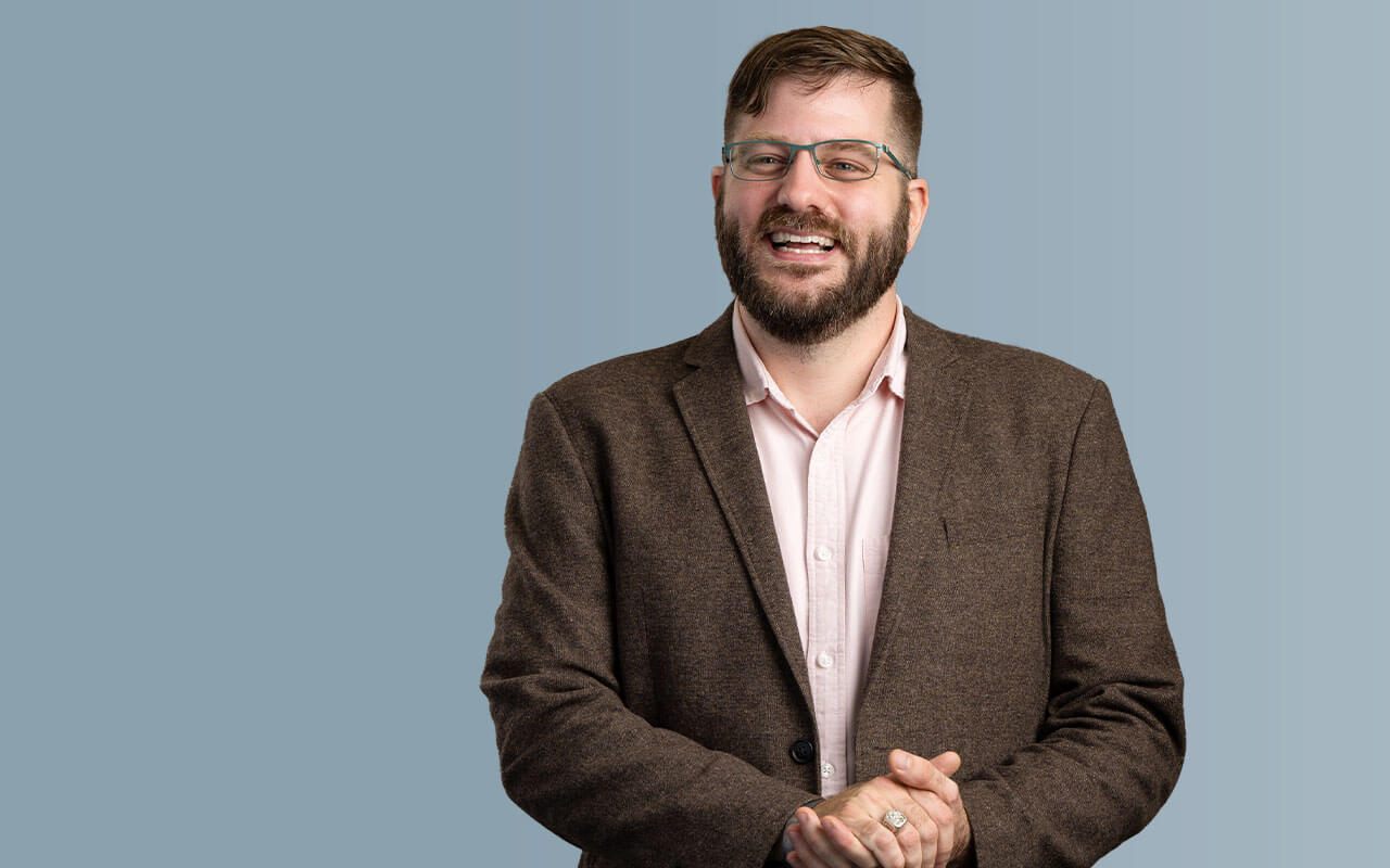 Guy Mattingly Weissinger II, selected as a Villanova Change-Maker, stands smiling with his hands held together. He wears glasses and appears confident and approachable.