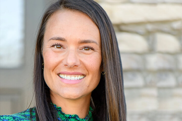 Headshot of Nikki Schultek smiling outdoors in front of a stone building.