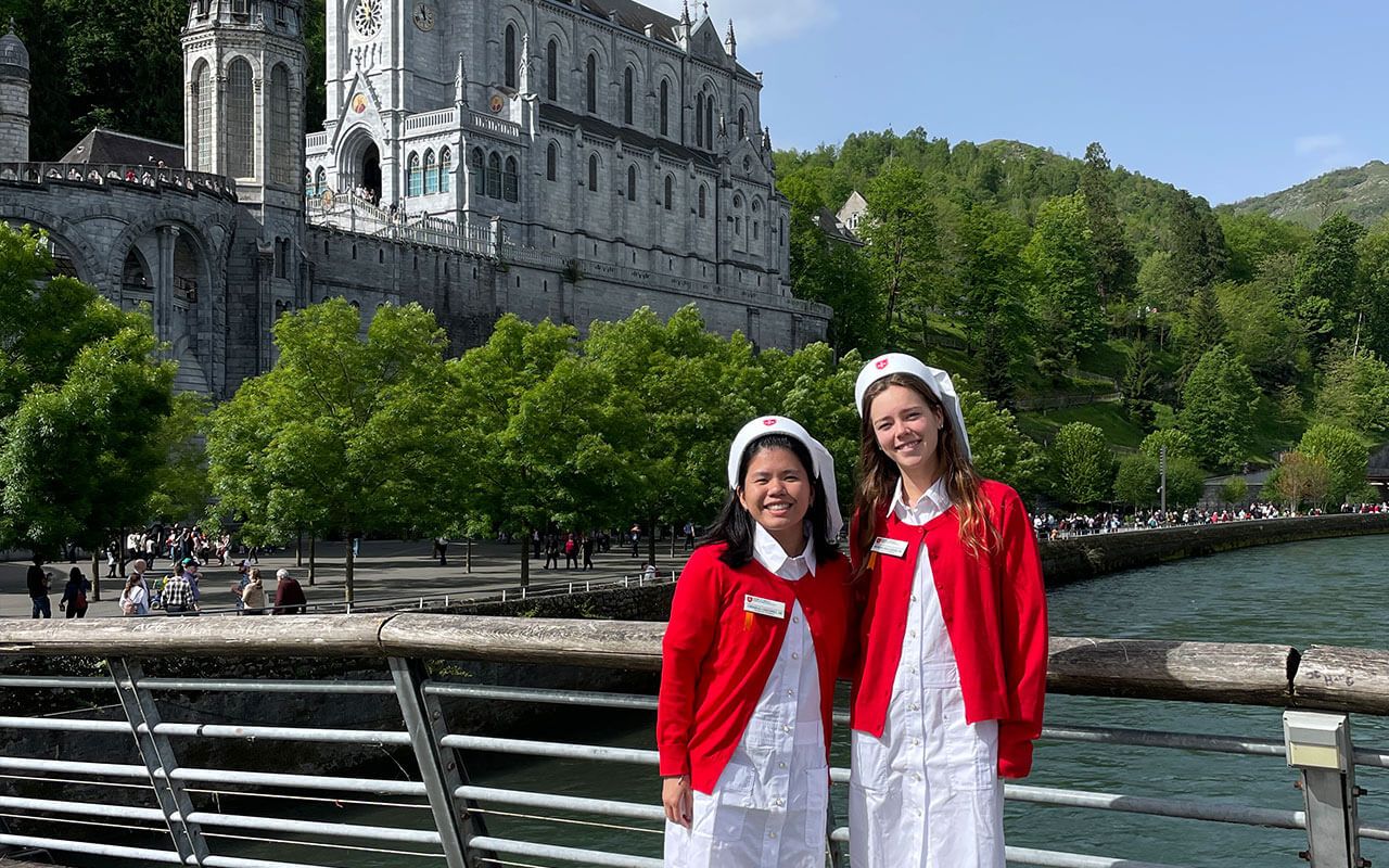 Crishelle Ildefonso and Peyton Shallcross, both Villanova Nursing students from the Class of 2026, pose in Order of Malta service uniforms in front of the Basilica of the Immaculate Conception at the Sanctuary of Our Lady of Lourdes.