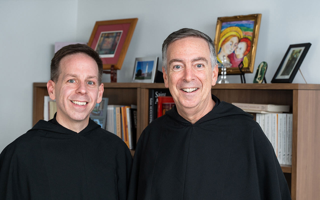 The Rev. Kevin DePrinzio and the Rev. Joseph L. Farrell stand side by side in front of a bookshelf, both wearing traditional black Augustinian robes.
