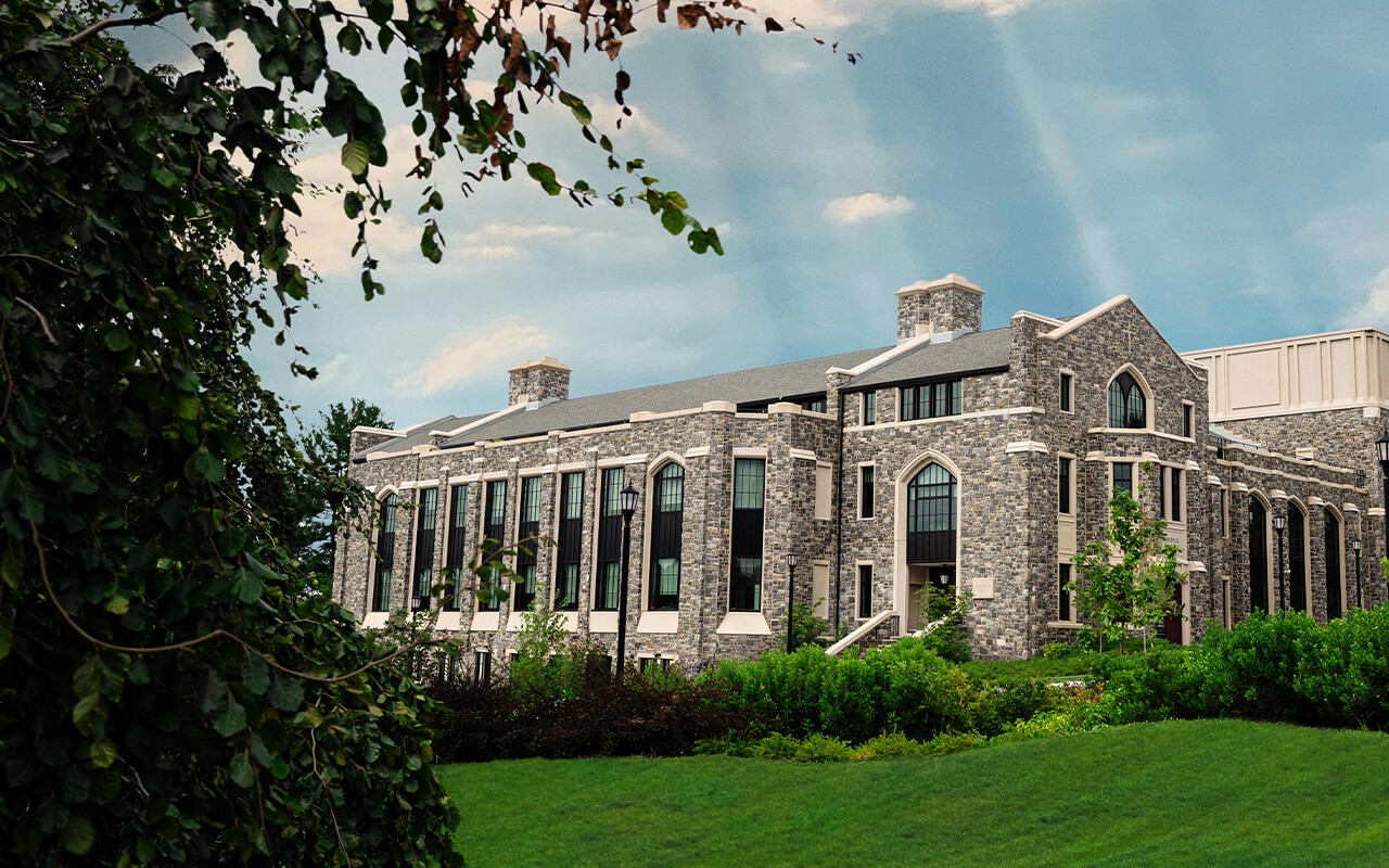 Exterior view of Drosdick Hall at Villanova University, surrounded by greenery including shrubs and young trees, under a clear blue sky, with the rooftop garden walls visible.