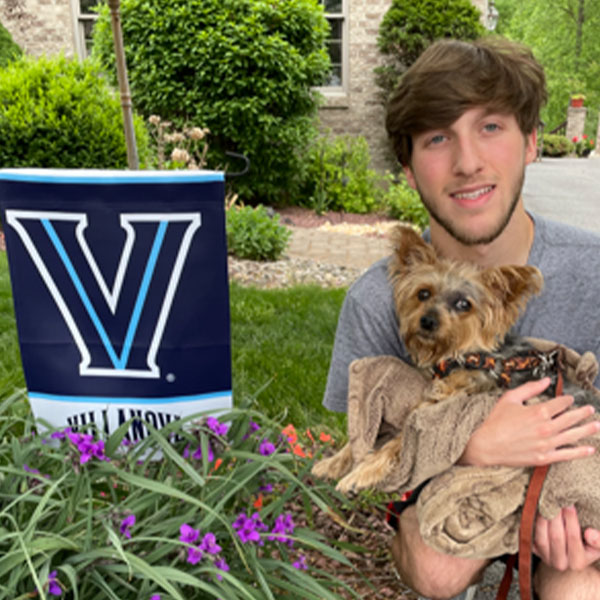 a young man holds a yorkie while kneeling next to a Villanova garden flag
