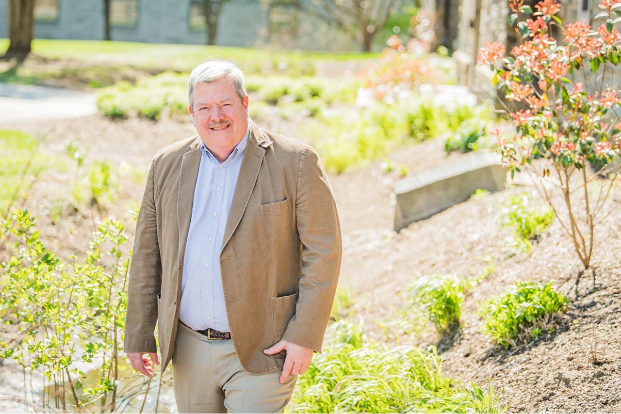 Robert Traver wearing a blazer and khakis standing outside in a green space