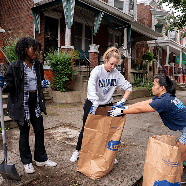 Three female students work together to fill brown paper lawn and leaf bags