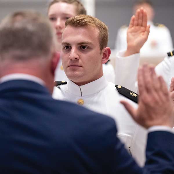 A group of service members in white dress uniforms stand with right hands raised.