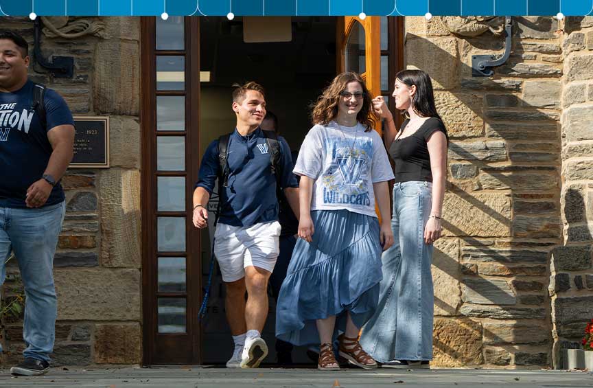 Students walk out of a campus building, with one holding the door open for others.