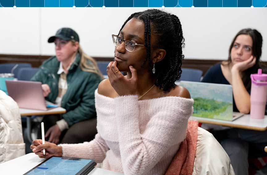 Students sit in a classroom while listening and taking notes.