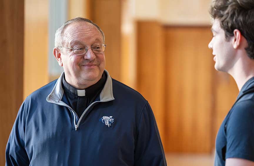 The Rev. Bernard C. Scianna, OSA, speaks with a student in an indoor campus setting.