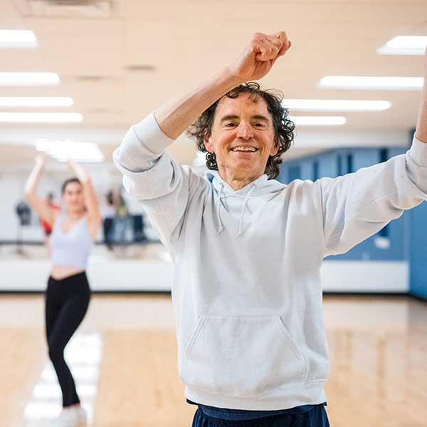 A person raises both arms while participating in a movement class inside a fitness studio.