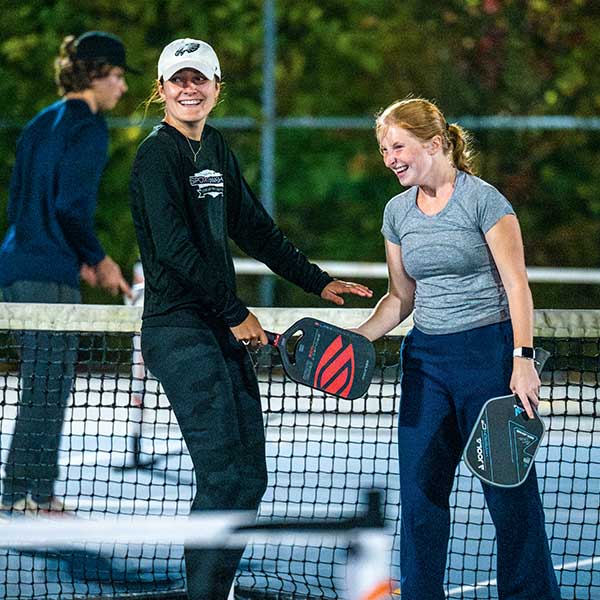 People stand on a pickleball court holding paddles near a net during a game.