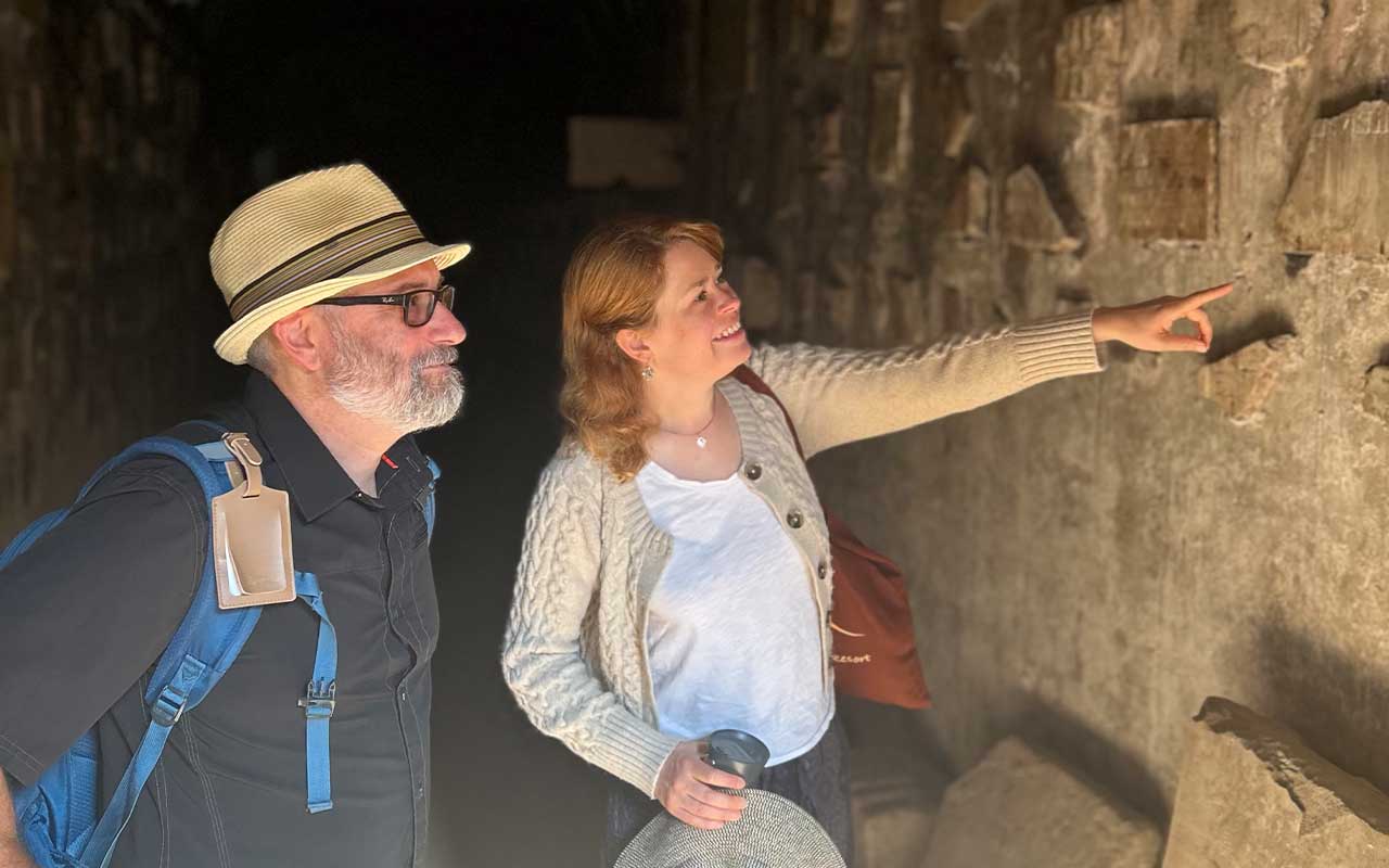 Two Villanova professors explore a stone corridor, with one person pointing toward details on the wall.