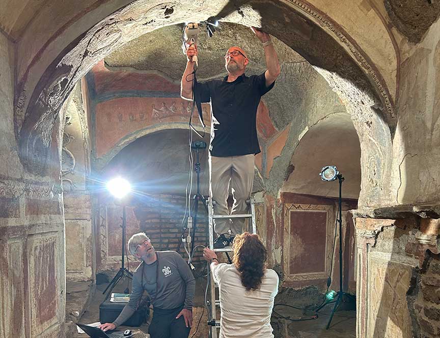 Researchers document frescoes inside an underground catacomb, using lighting equipment to examine and record painted surfaces on the arched ceiling
