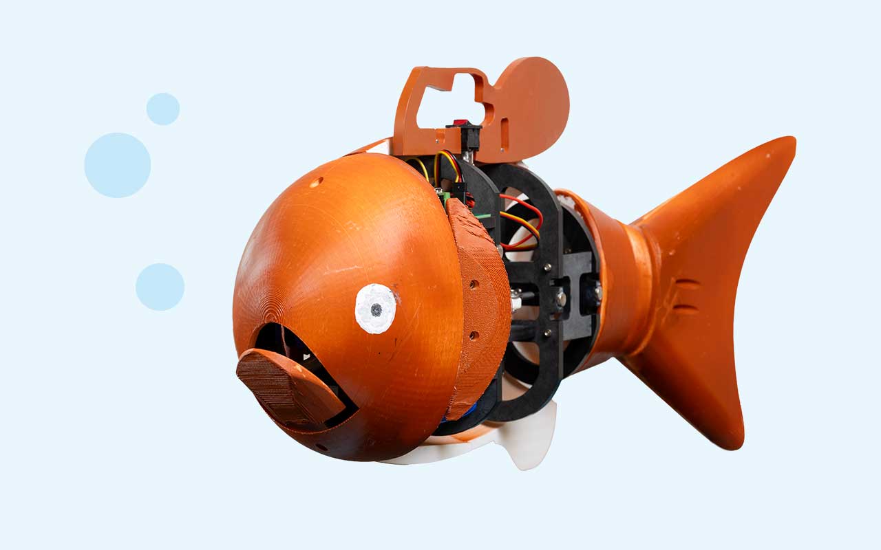 A robotic goldfish with an orange body releases air bubbles from its mouth, revealing exposed mechanical components.